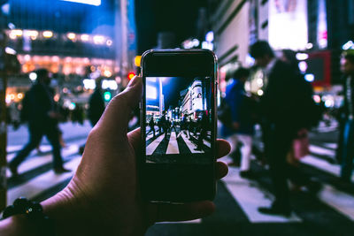 Copped hand of person photographing crowd on zebra crossing at night