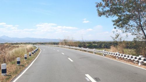 Empty road by field against sky