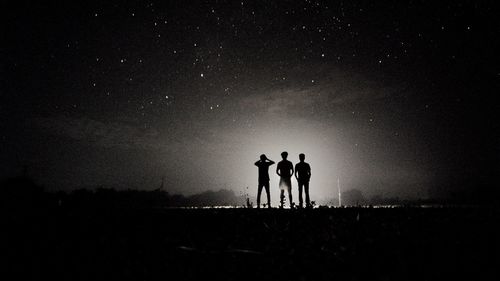 Silhouette friends standing on landscape against sky at night