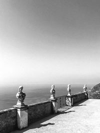 Sculpture on retaining wall by sea against clear sky