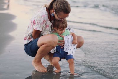 Rear view of mother and cute blonde baby boy on the beach touching the sea for the first time