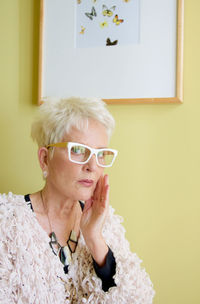 Portrait of serious senior woman against picture frame mounted on wall