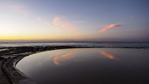 Scenic view of infinity pool by sea against sky during sunset