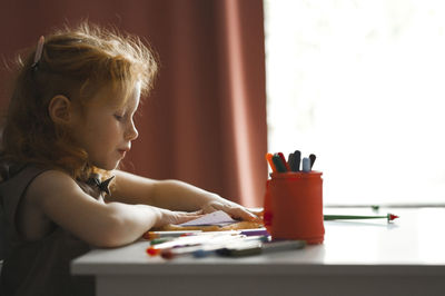 Girl drawing on paper sitting at desk in home