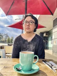 Portrait of young asian man having hot coffee at sidewalk cafe under red cafe umbrella.