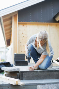 Full length of woman using cordless screwdriver nail into floorboard