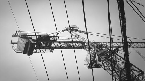 Low angle view of crane and cables against sky