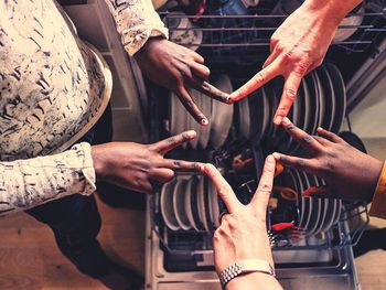 High angle view of friends making star shape with hands over plates in dishwasher