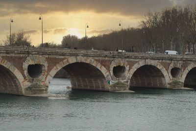 Arch bridge over river against sky during sunset