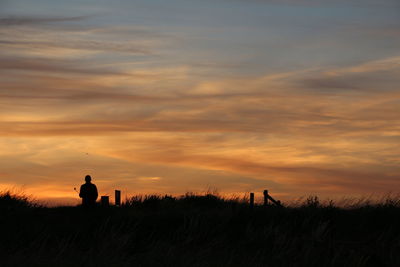 Silhouette man standing on field against sky during sunset