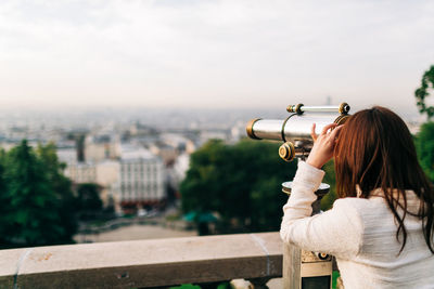 Rear view of woman looking at cityscape against sky