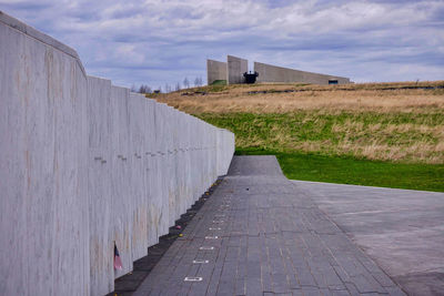 Footpath by wall against sky