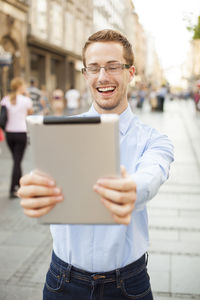 Portrait of a smiling young man holding smart phone in city