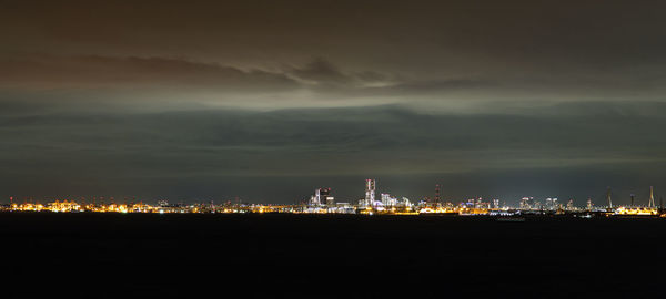 Illuminated city by buildings against sky at night