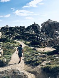 Rear view of man walking on rock against sky