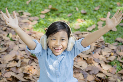 Portrait of happy girl with arms raised wearing ear muff in park