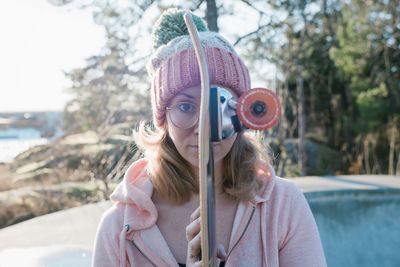 Portrait of a woman holding her skateboard in front of her face