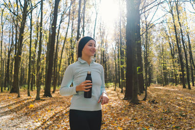 The girl drinks water. a beautiful girl is doing fitness outdoors in a sunny autumn forest