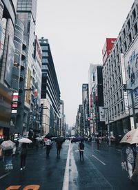 People walking on city street amidst buildings against sky