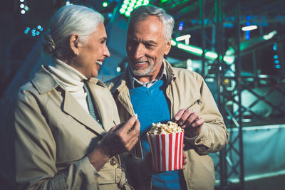Smiling couple eating popcorn while standing at carnival