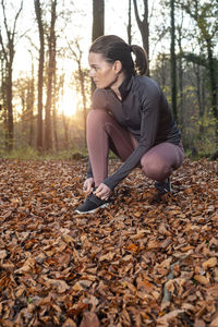 Sporty woman tying up her shoelace before running through the forest