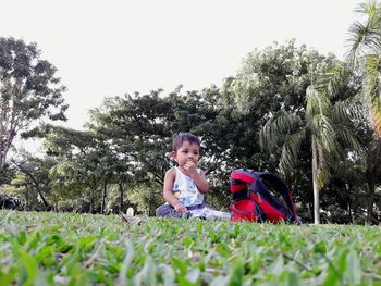 Toddler sitting by bag on grass against trees at park