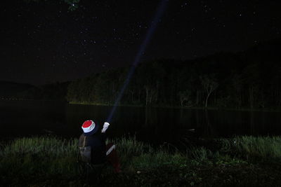 Man standing on field by lake against sky at night