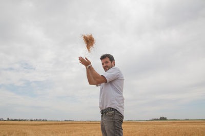 Portrait of smiling farmer throwing crops while standing on field