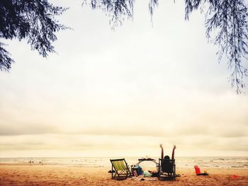 People sitting on beach by sea against sky