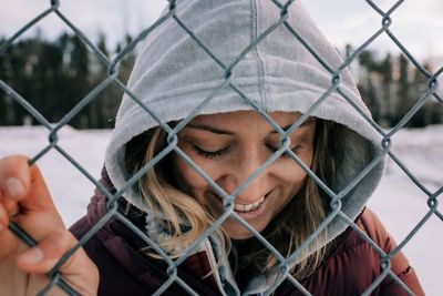 Portrait of woman smiling holding onto a metal fence with hood up