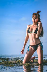 Woman in bikini knelling at beach against sky