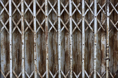 Full frame shot of rusty metal fence against wall