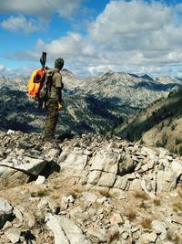 Side view of hiker standing on rocky mountain against cloudy sky