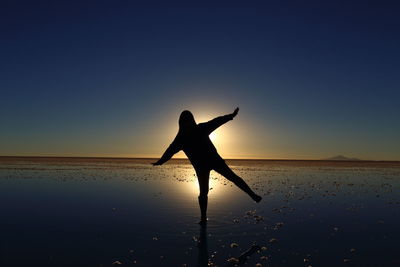 Silhouette woman standing at beach against sky during sunset