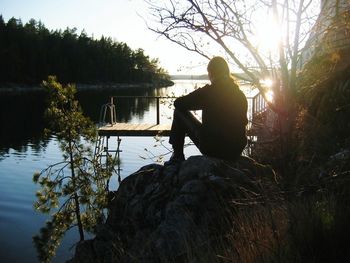 Silhouette man sitting by lake against sky during sunset