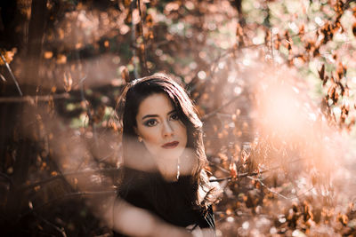 Portrait of young woman standing against tree