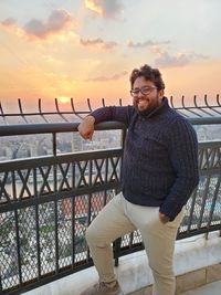 Portrait of young man standing against railing during sunset