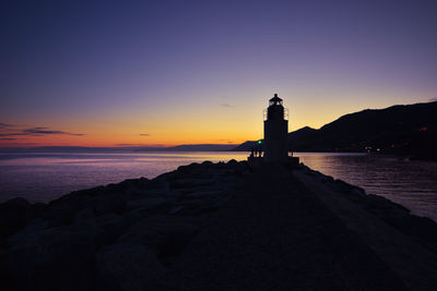 Lighthouse by sea against sky during sunset