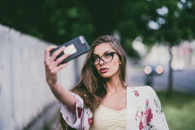 Beautiful young woman taking selfie using mobile phone in city