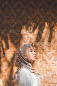Side view of woman in hijab standing against patterned wall outdoors