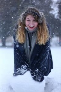 Portrait of smiling young woman on field during snowfall