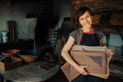 Smiling female craftsperson holding wooden panels in workshop