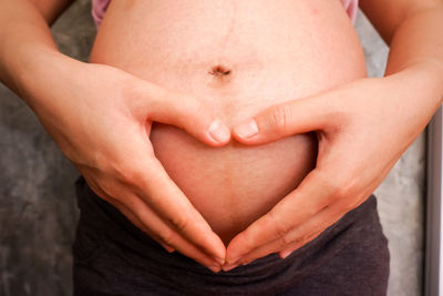 Midsection of pregnant woman making heart shape on stomach