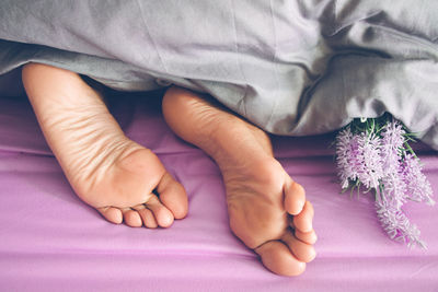 Low section of man by flower lying under blanket on bed