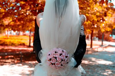 Rear view of bride embracing groom with bouquet on field