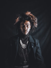 Portrait of young man standing against black background