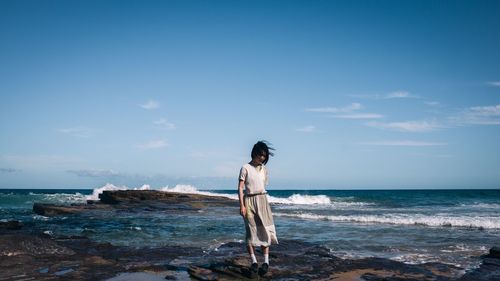 Woman standing on rock at beach against sky