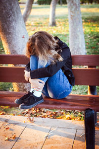 Sad teenager girl sitting on the bench in autumn park. crying young girl in depression
