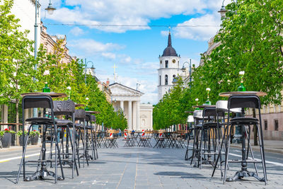 Empty chairs and table by buildings in city against sky