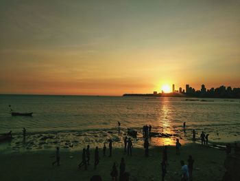 Silhouette people on beach against sky during sunset